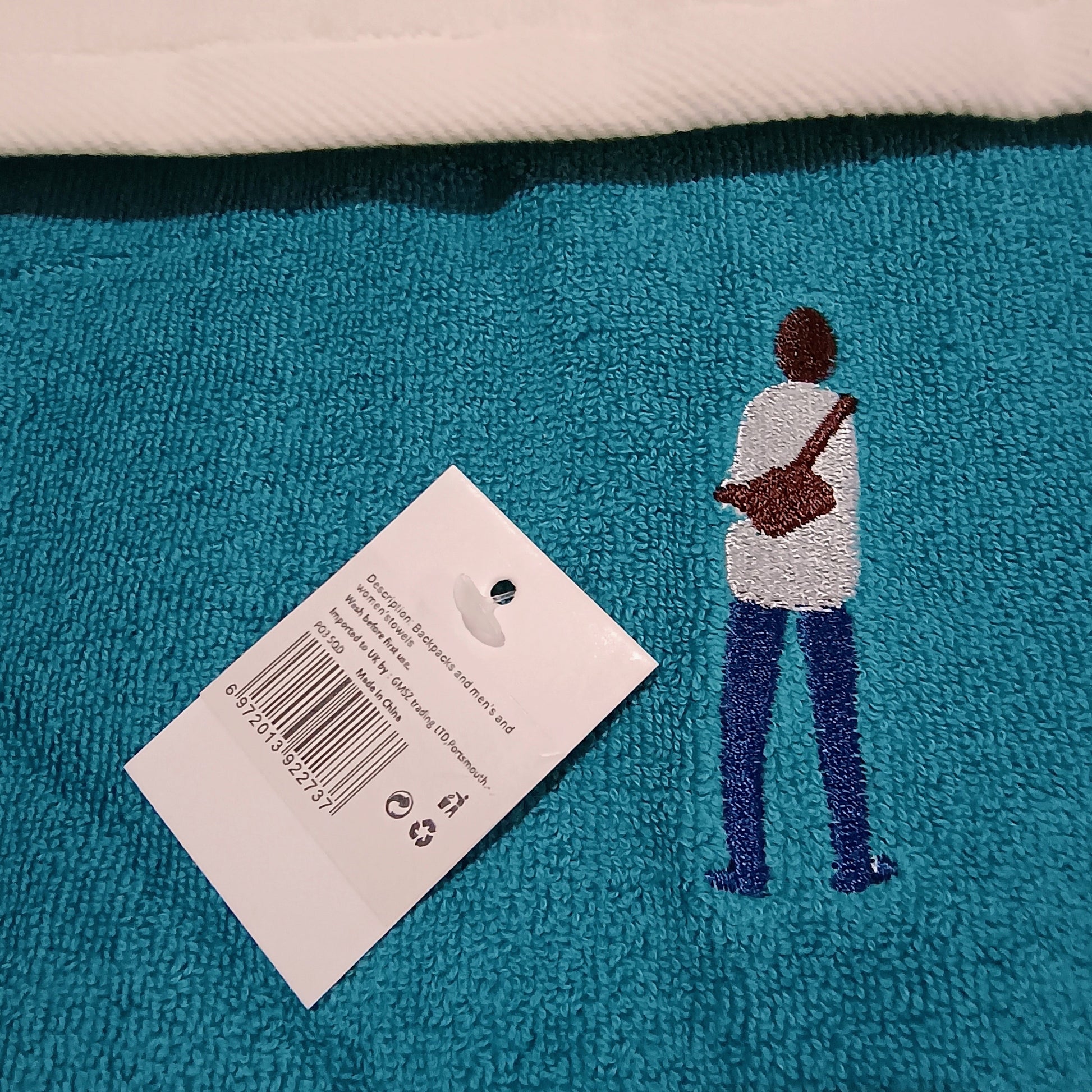 Teal rug with embroidered silhouette of a person holding a bag and a tag.
