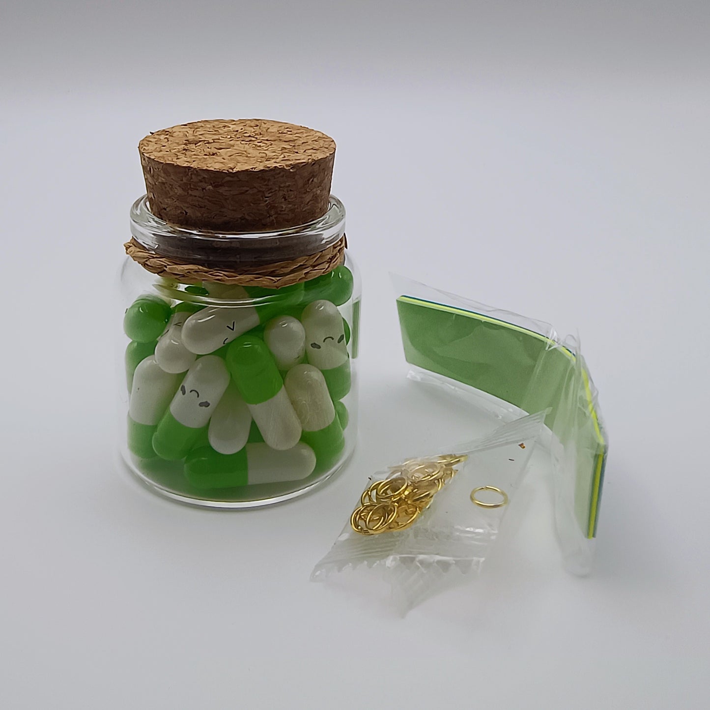Glass jar with green and white decorative items, gold chain, and clear packaging on a white background