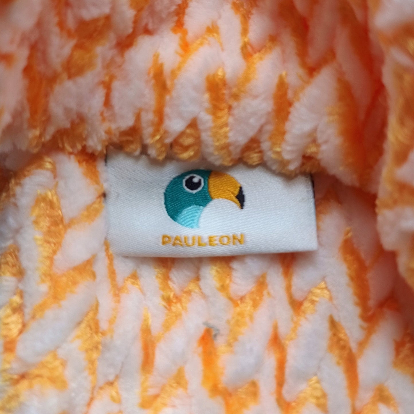 Close-up of a fluffy orange and white textured fabric with a brand label featuring a cartoon character.