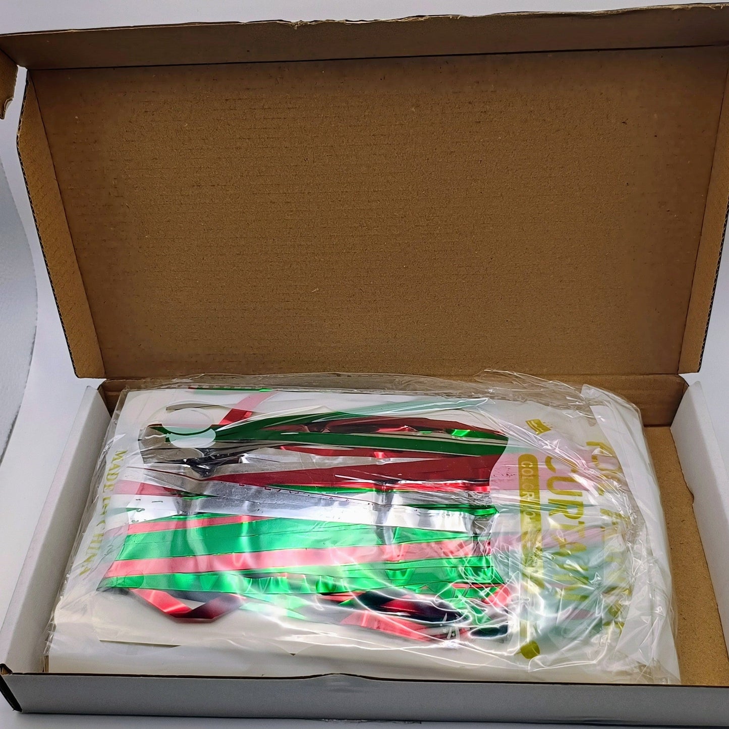 Open cardboard box with a plastic bag containing colorful items on a white background
