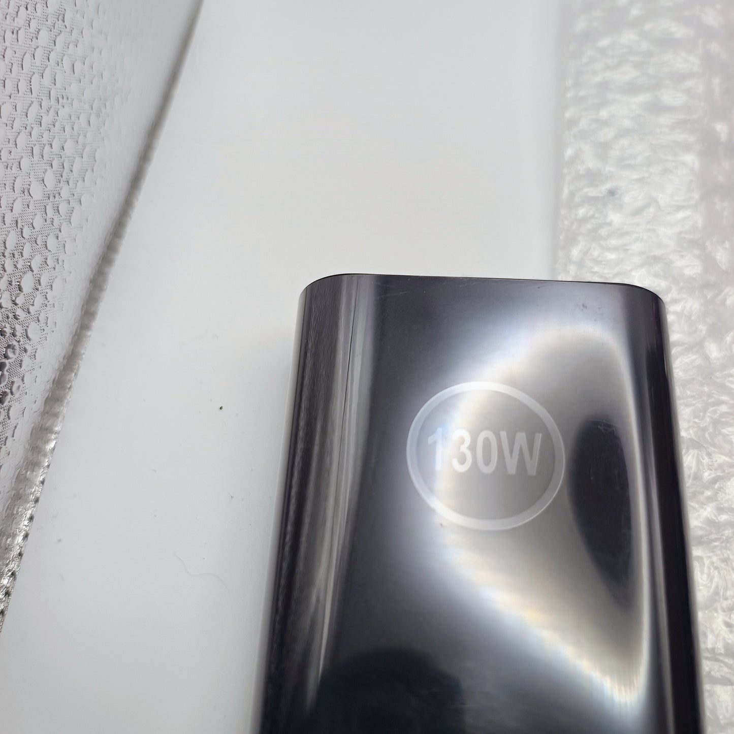Chrome power adapter with '130W' marking on a textured white background