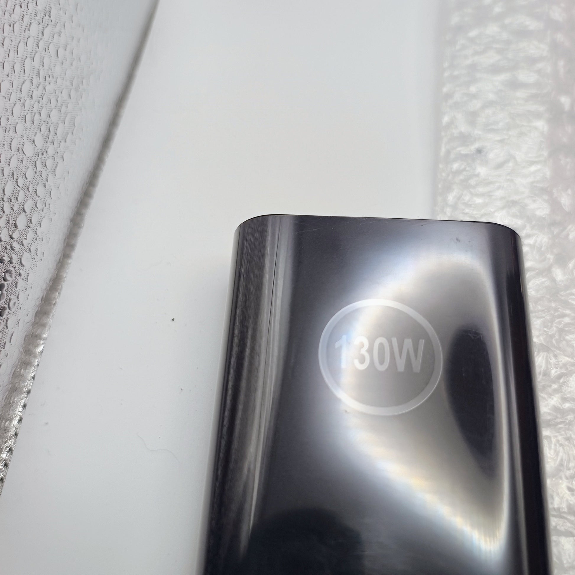 Chrome power adapter with '130W' marking on a textured white background