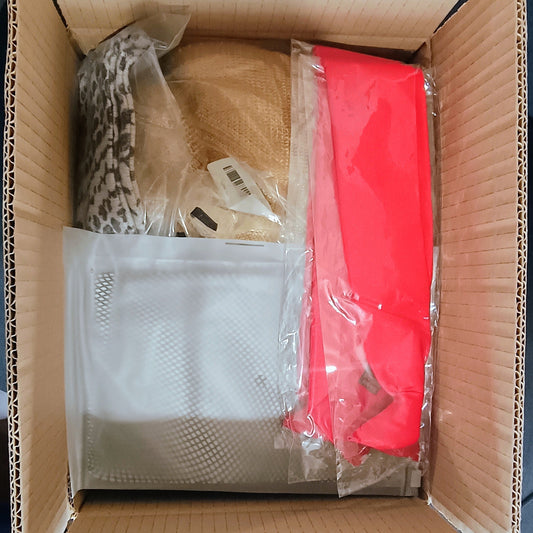Open cardboard box with various items including a white mesh bag, red item, and others.