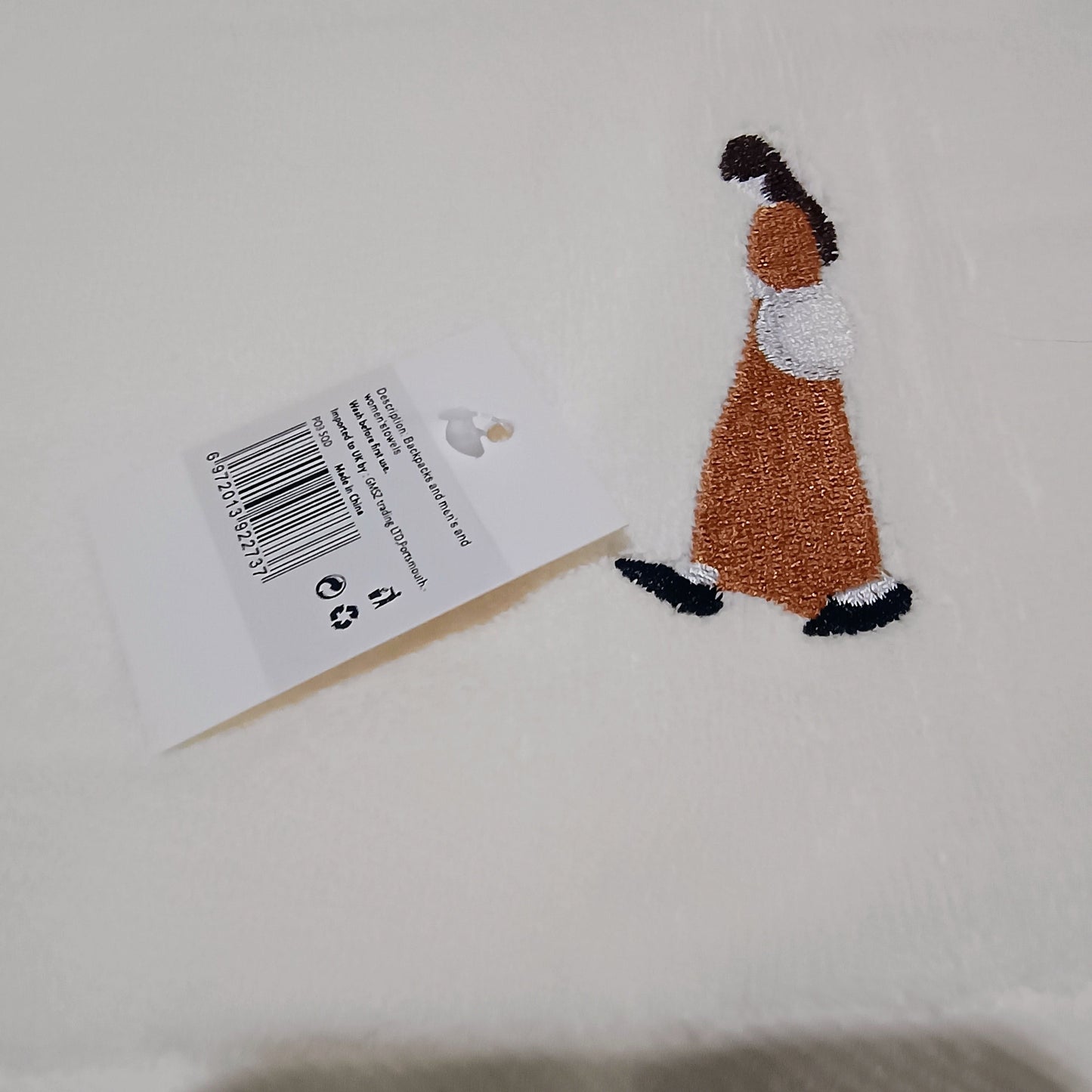 Embroidered patch of a person in a dress on a beige background with a tag.