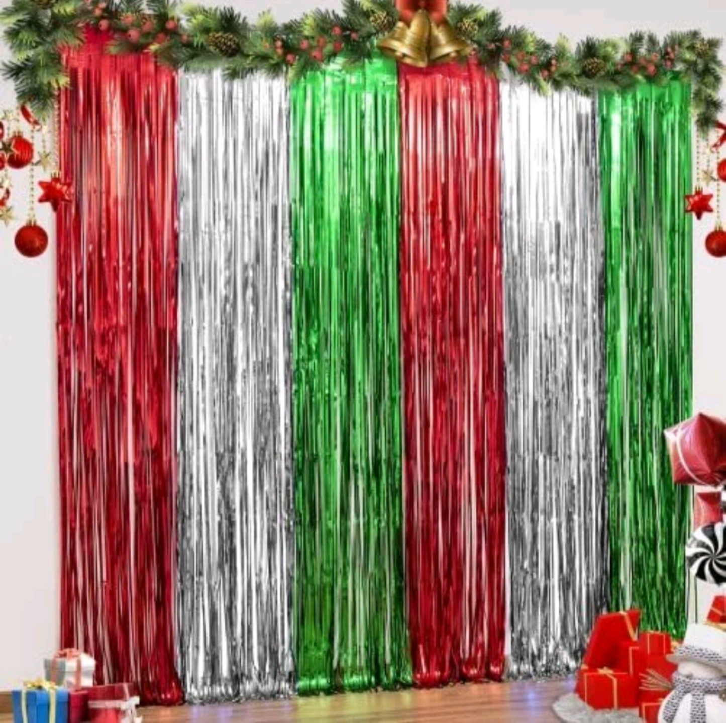 Colorful tinsel curtains in red, green, and silver with Christmas decorations on a white wall.